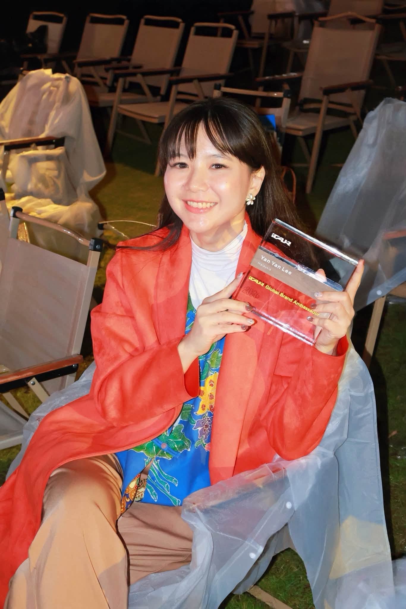 Yan Yan Lee holding an award inscribed with her name and iCAUR Global Brand Ambassador.